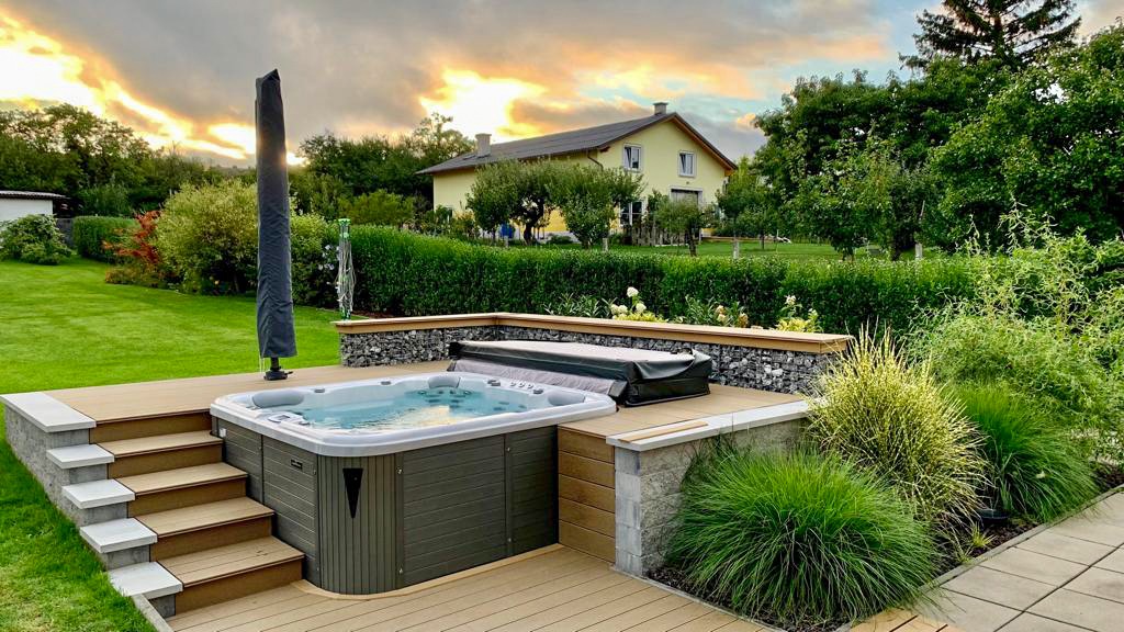 Whirlpool auf erhöhter Holzterrasse mit Gartenblick, umgeben von Ziergräsern bei warmem Abendlicht.