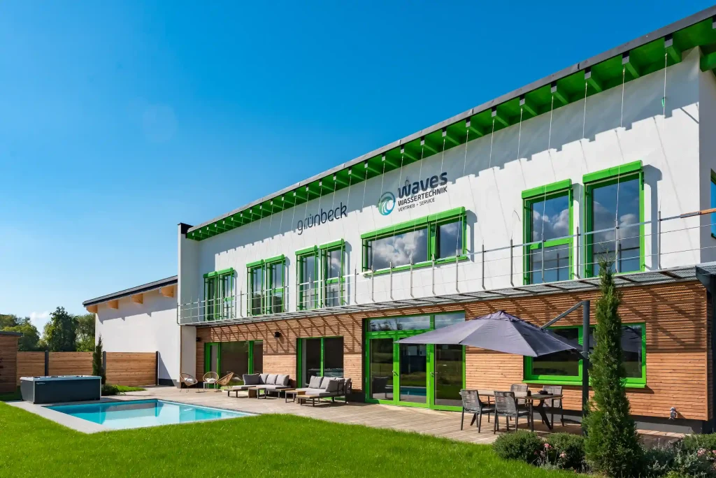 Modernes Firmengebäude von Waves Wassertechnik mit Terrasse, Pool und grüner Fensterrahmung bei Sonnenschein.