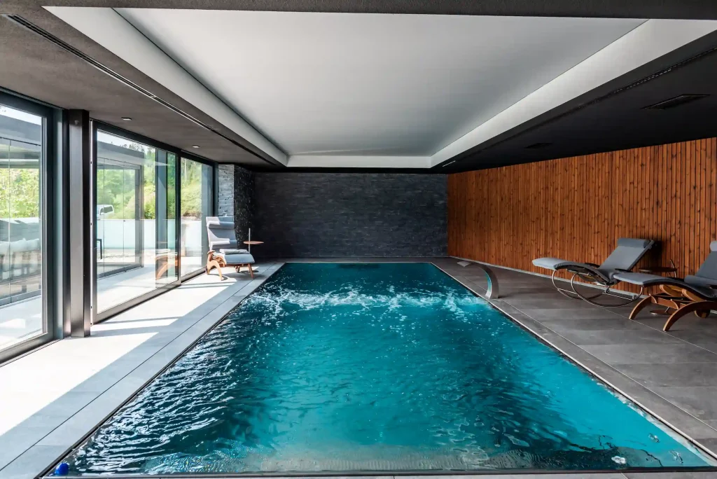 Moderner Indoor-Pool mit Glasfront, Holzverkleidung und Liegen in elegantem Wellnessbereich.