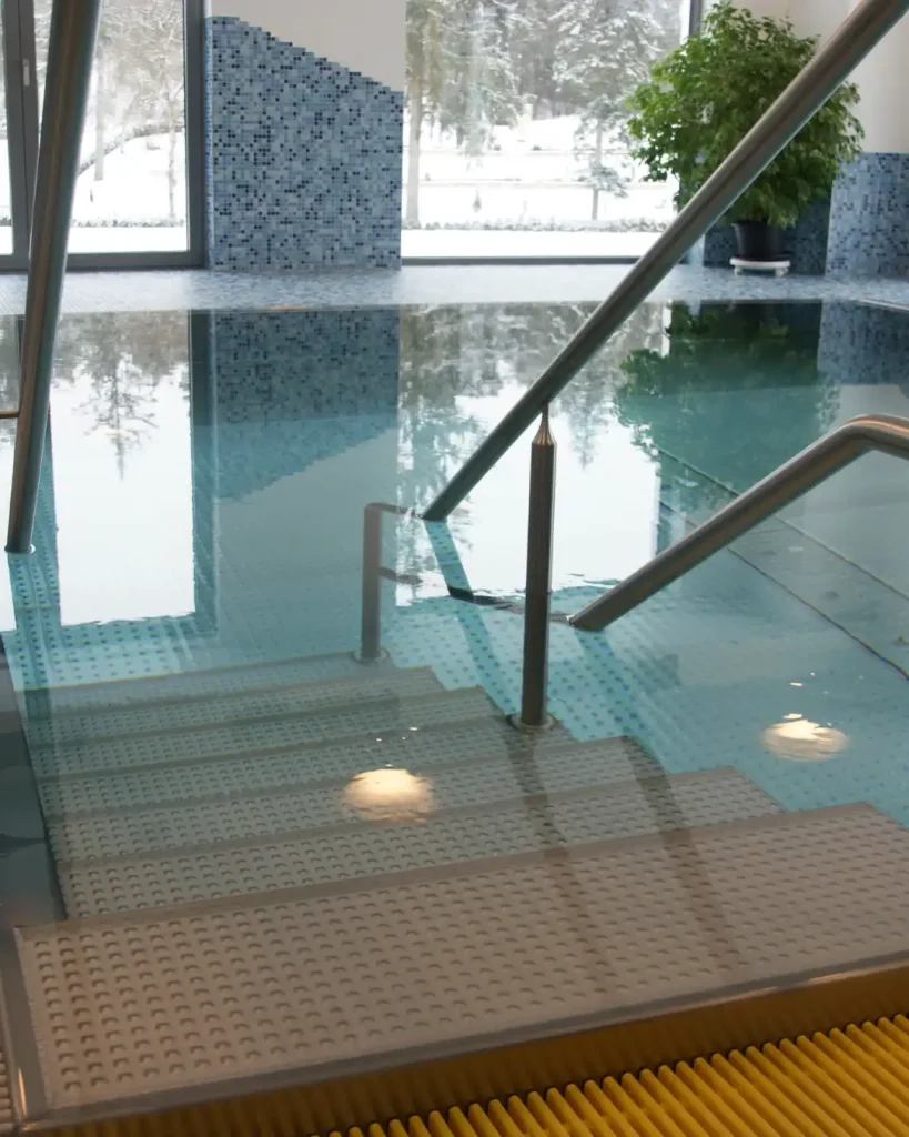 Hallenbad mit Treppeneinstieg aus Edelstahl und hellblauen Mosaikfliesen mit Panoramablick.