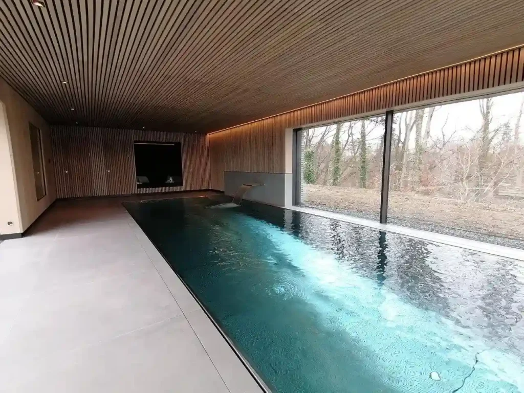 Eleganter Innenpool mit Holzdecke und Panoramafenstern – stilvolles Spa-Ambiente mit Blick ins Grüne.