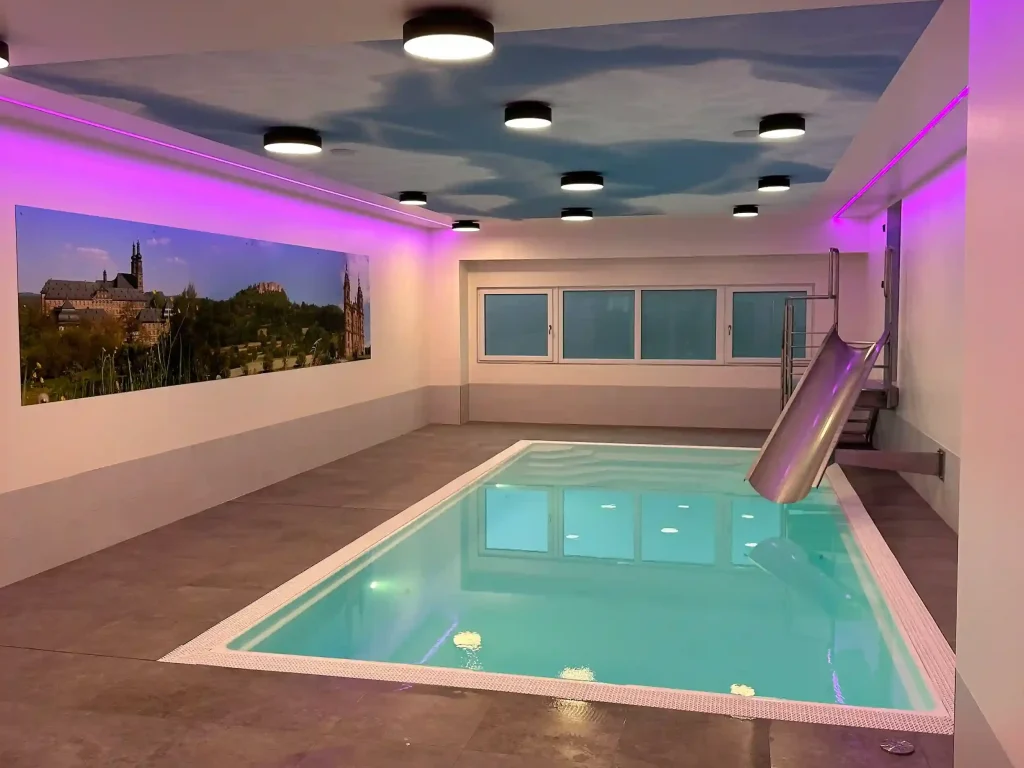 Beleuchteter Innenpool mit Wasserrutsche und Wandbild, moderne Deckenbeleuchtung in violettem Licht.