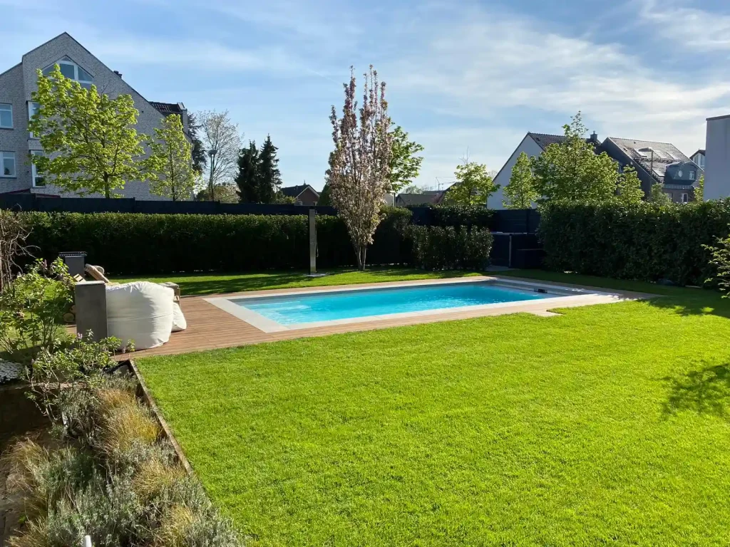 Moderner Garten mit kleinem Pool und Holzterrasse – gepflegter Rasen, Hecken und junge Bäume im Wohngebiet.