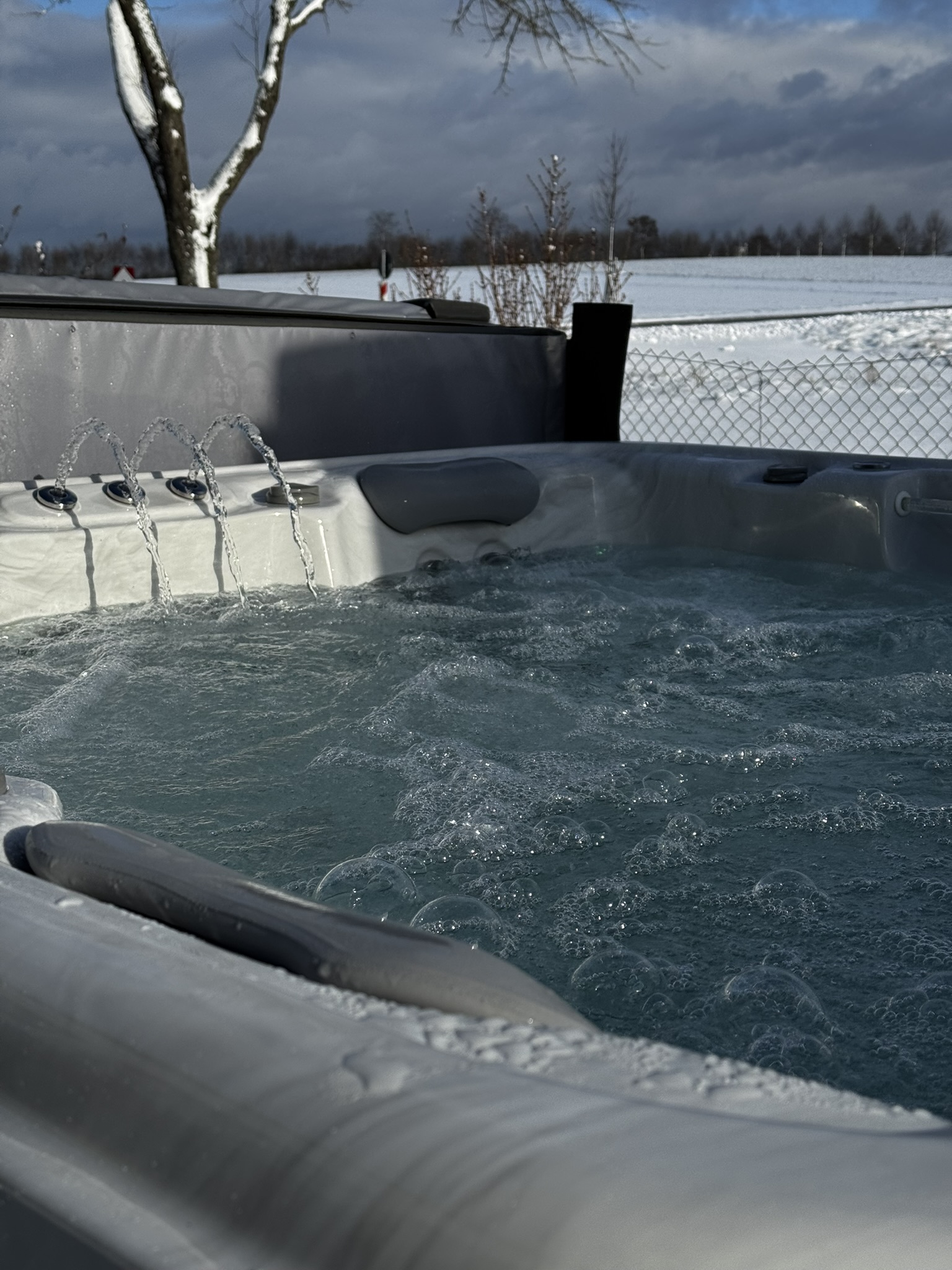 Nahaufnahme eines Whirlpools in winterlicher Landschaft. Wasserattraktionen sind eingeschaltet.
