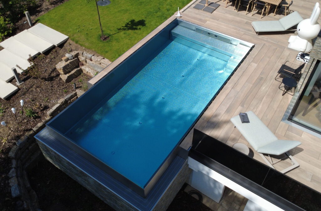 Exklusiver Edelstahlpool im Garten mit Infinity-Kante und tiefer Überlaufrinne. Modernes Design, perfekter Wasserspiegel und luxuriöses Badeerlebnis.
