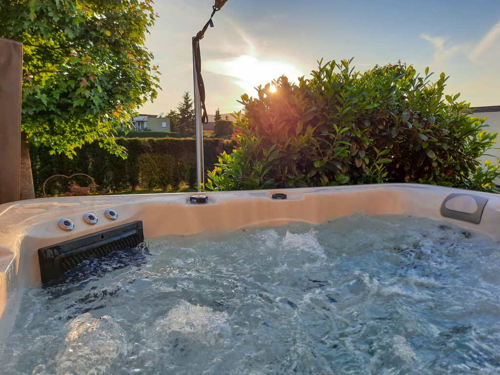 Sprudelnder Whirlpool mit Grünpflanzen im Hintergrund bei Sonnenuntergang.