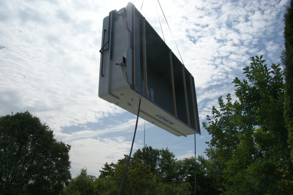 GFK-Becken in der Luft an Kran zur Anlieferung. Becken hängt hochkant in der Luft.