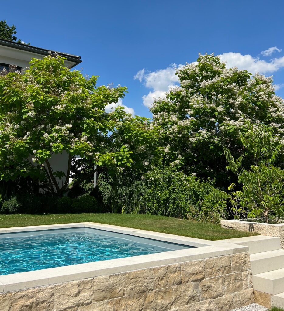 Teile eines Gartenpools  umgeben von Bäumen und Rasen bei strahlendem Sommerwetter.