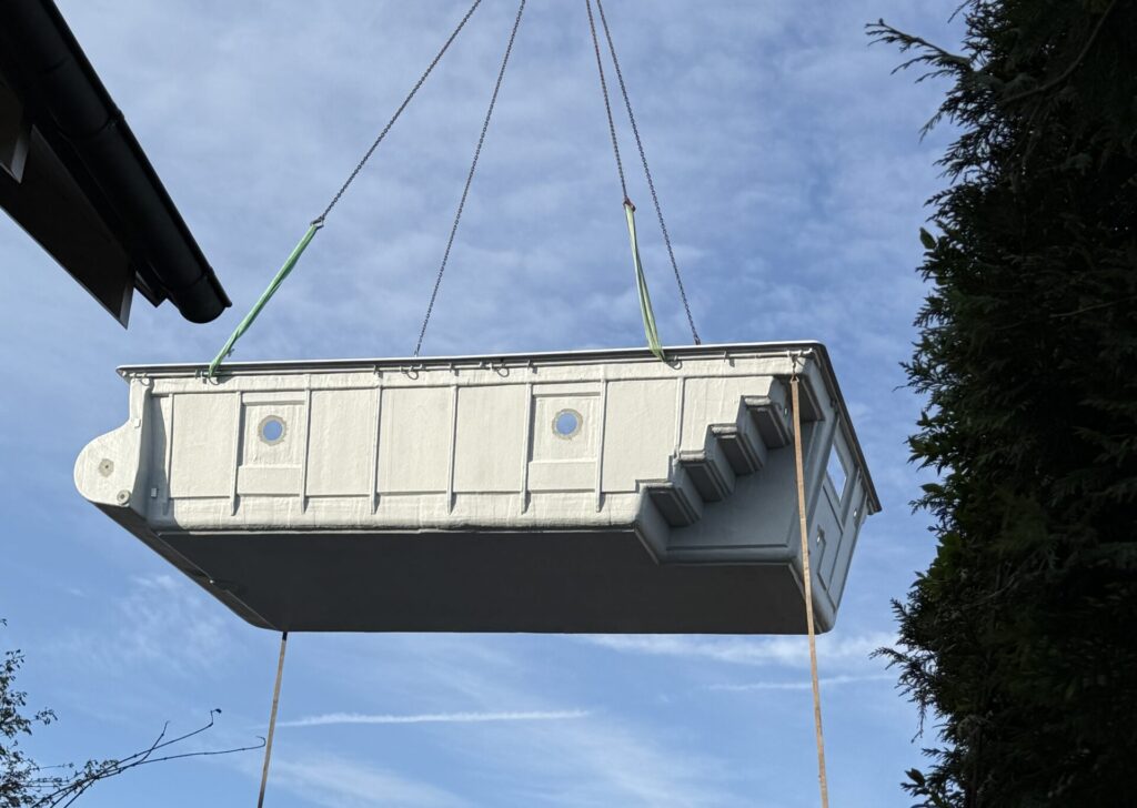Fertigbecken an 4 Haltepunkten in der Luft für die Platzierung mit Kran. Zu sehen sind die Aussparungen für die Scheinwerfer und die seitliche Blocktreppen.